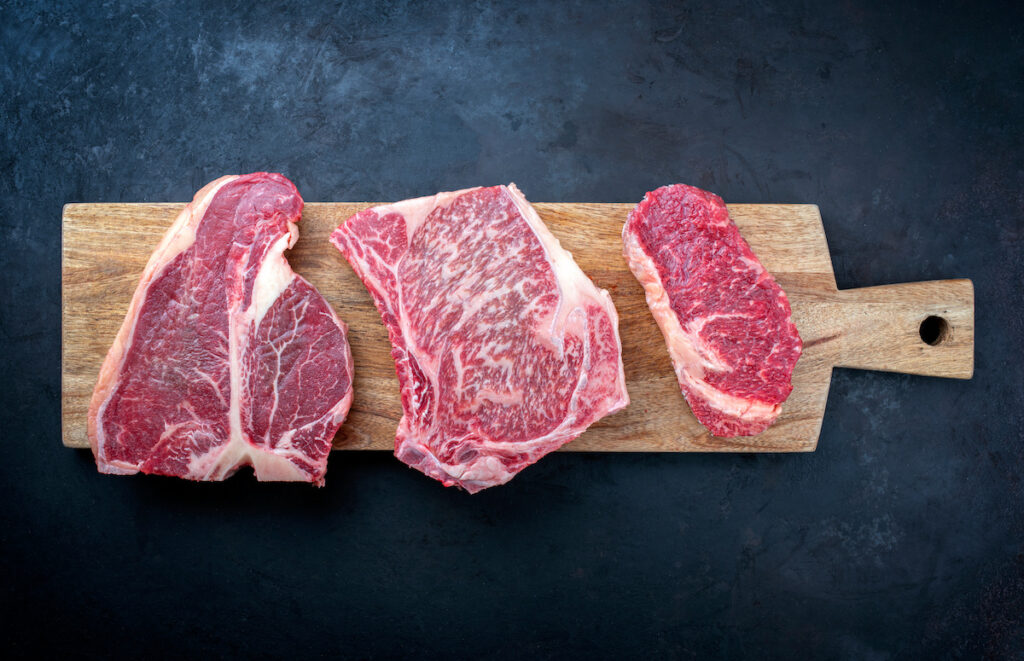 Raw dry aged wagyu porterhouse beef steak, entrecote and cutlet offered as top view on wooden board with copy space