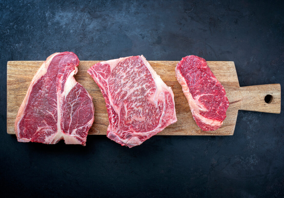 Raw dry aged wagyu porterhouse beef steak, entrecote and cutlet offered as top view on wooden board with copy space